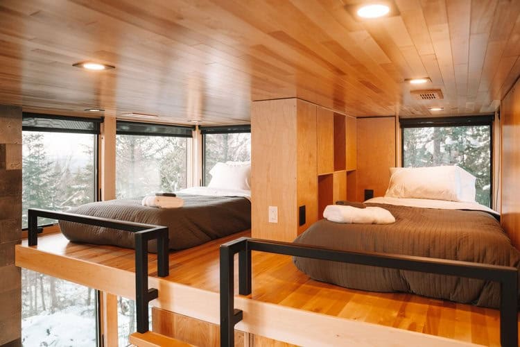 Compact tiny house bedroom with large windows and cozy sleeping areas.