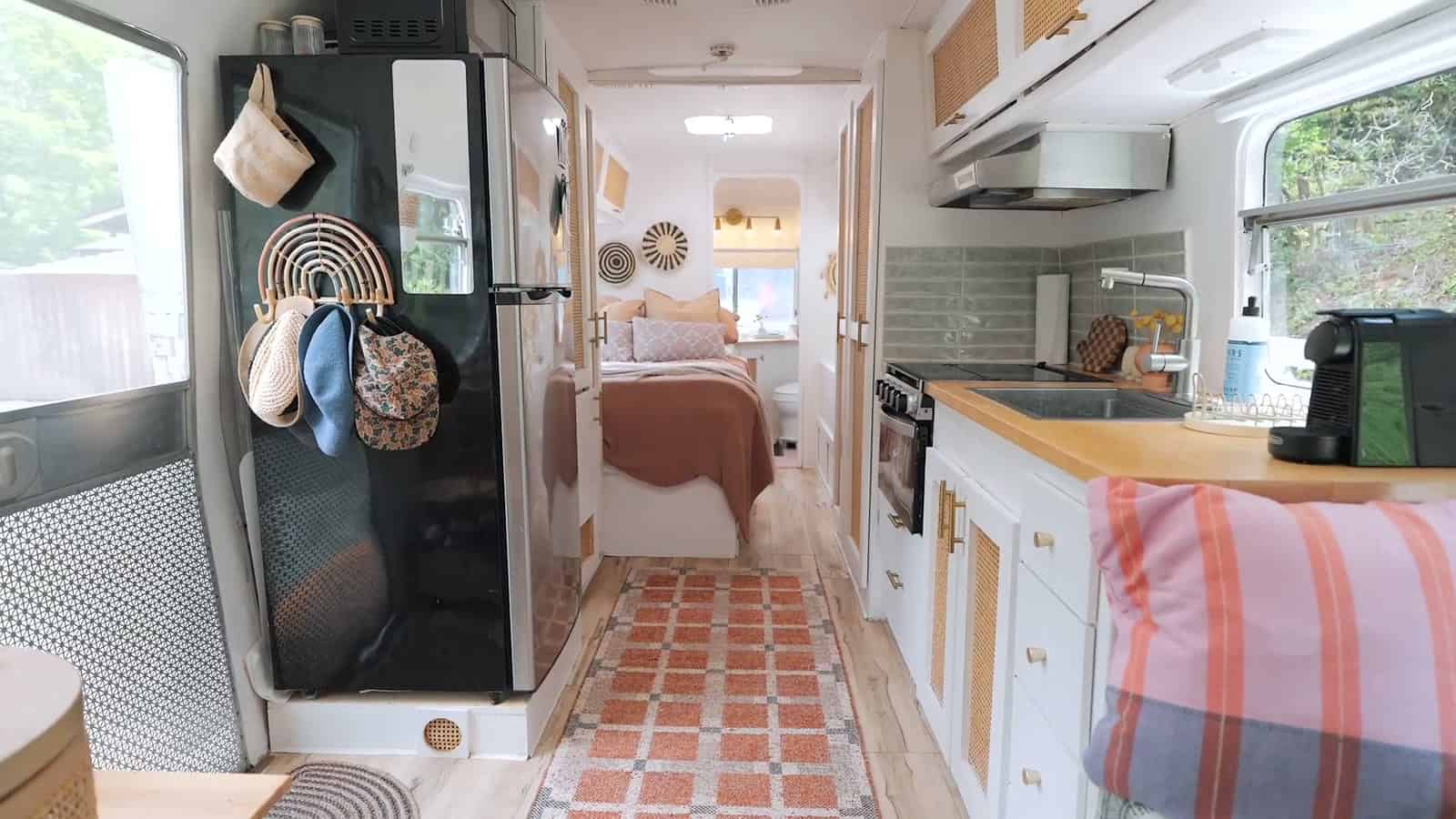 Renovated Avion interior looking down the hallway past a black refrigerator and white kitchen cabinets with a wood counter, a pink checkered runner on the floor and the bedroom at the far end