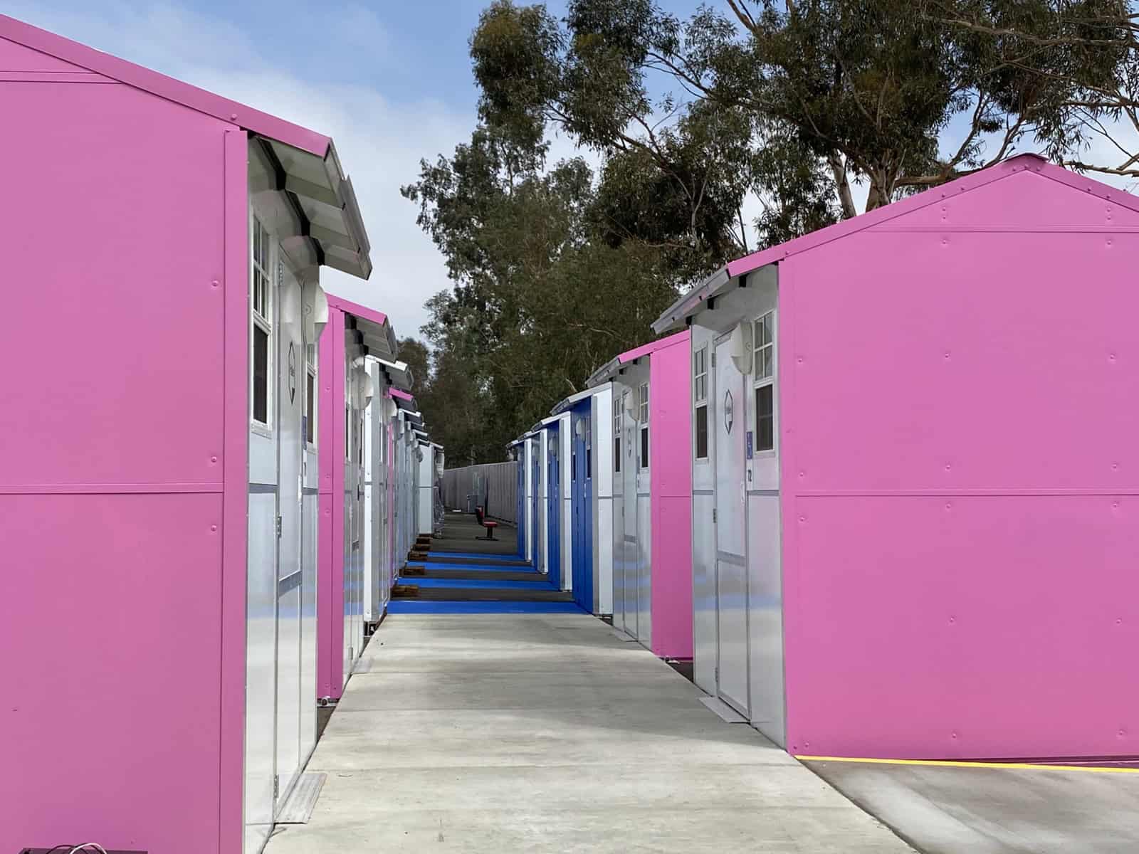 Rows of pink and blue Pallet tiny homes along a concrete path at the Saticoy Whitsett tiny home village in Los Angeles