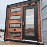 Portable sauna in a shipping container with modern black door and windows.