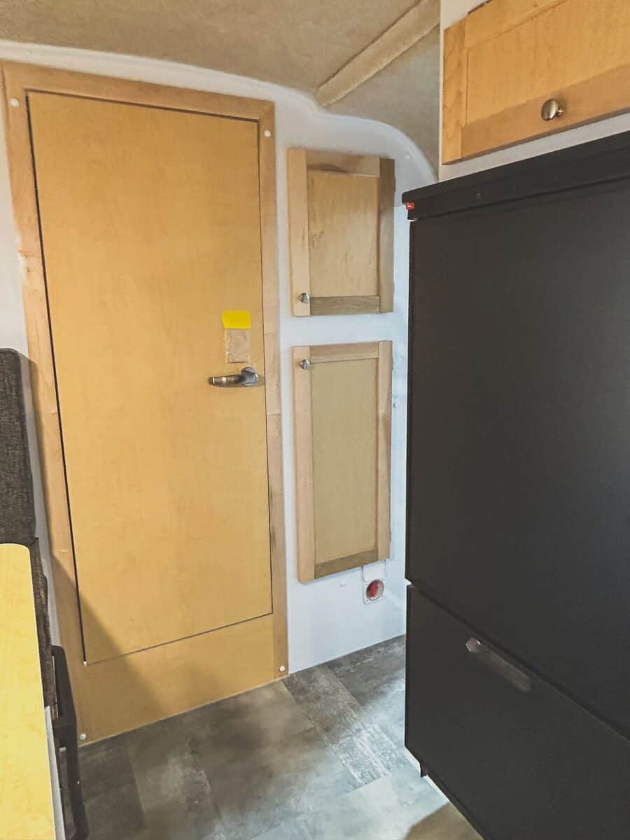 Wood bathroom door beside a black refrigerator