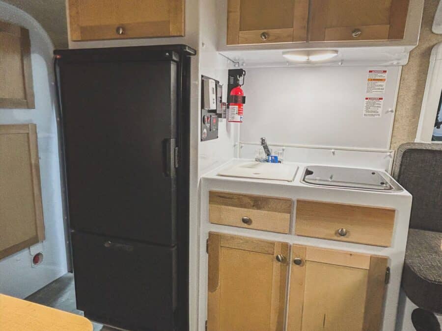 Black refrigerator next to a white galley with maple drawers
