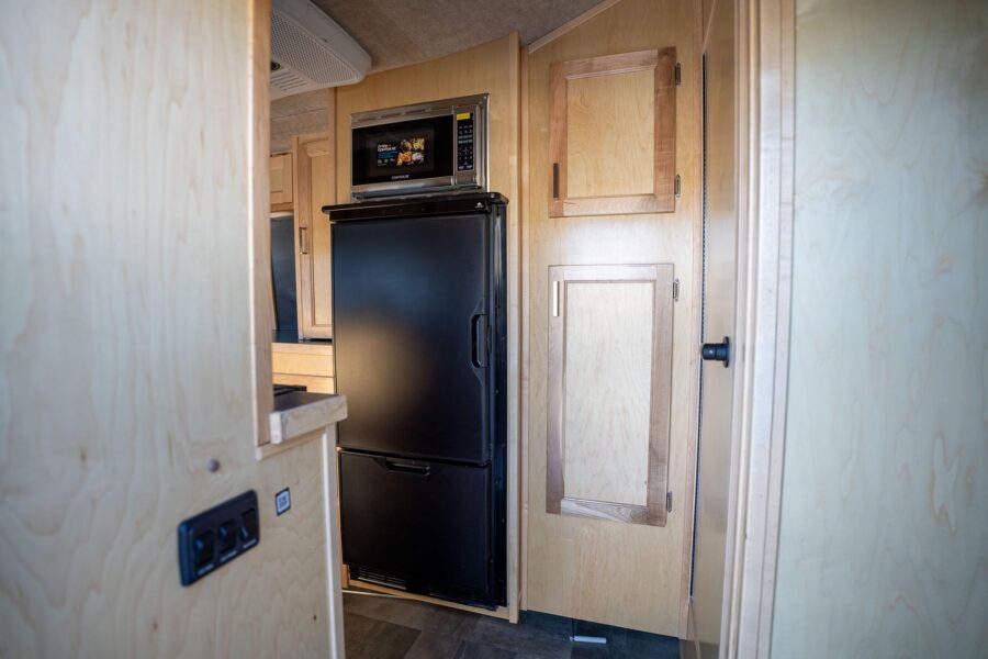 Tall refrigerator below a microwave beside closet doors