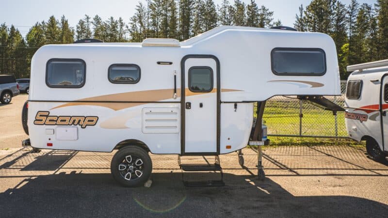 White Scamp 19 fifth wheel with tan stripes on a sunny lot