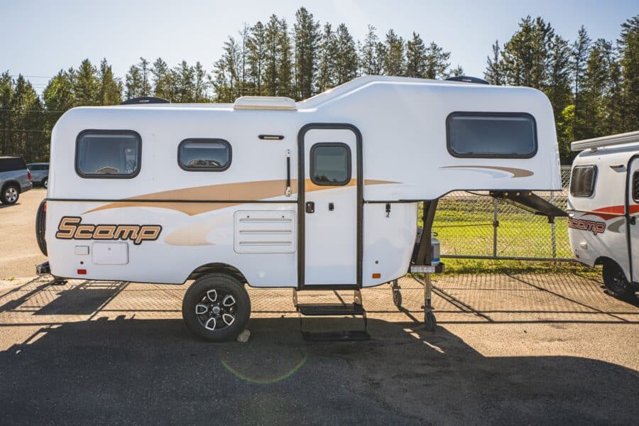 White Scamp 19 fifth wheel with tan stripes on a sunny lot