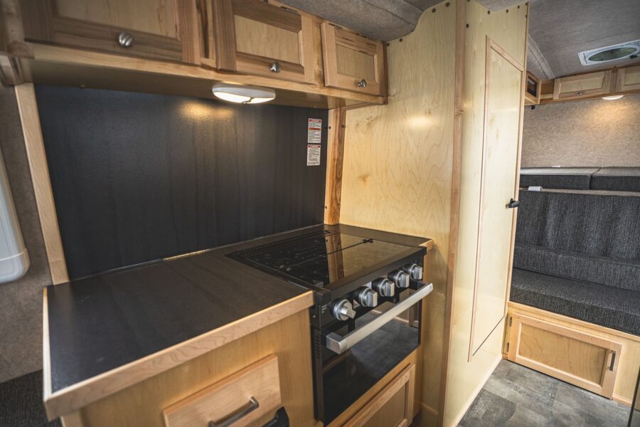 Stovetop and oven beside a tall maple cabinet