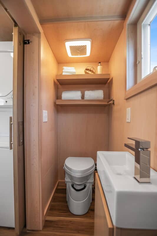 Small bathroom in a tiny house with wooden walls, shelves, and a compact toilet and sink.