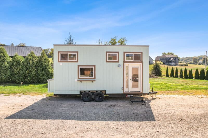 Tiny house on wheels with modern design and large windows in a scenic rural area.