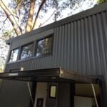 Modern tiny house with black metal exterior in a wooded setting.