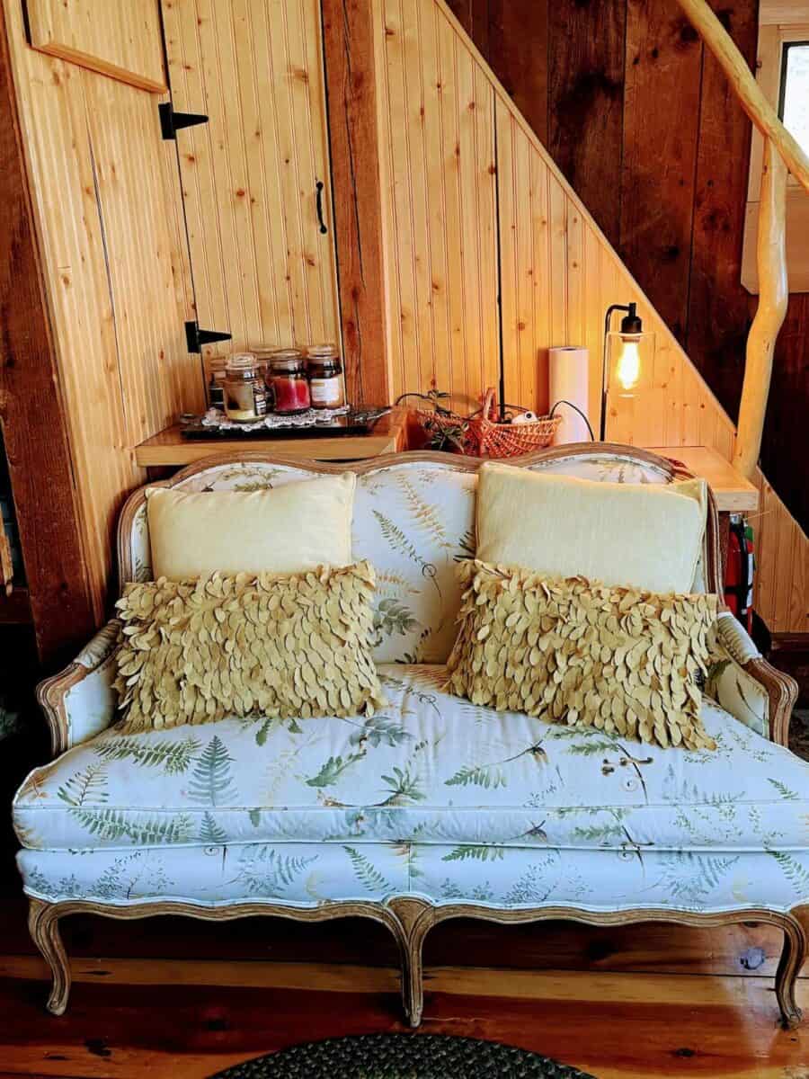 Charming rustic cabin living space featuring a vintage sofa with plush pillows, wooden walls, and wa.