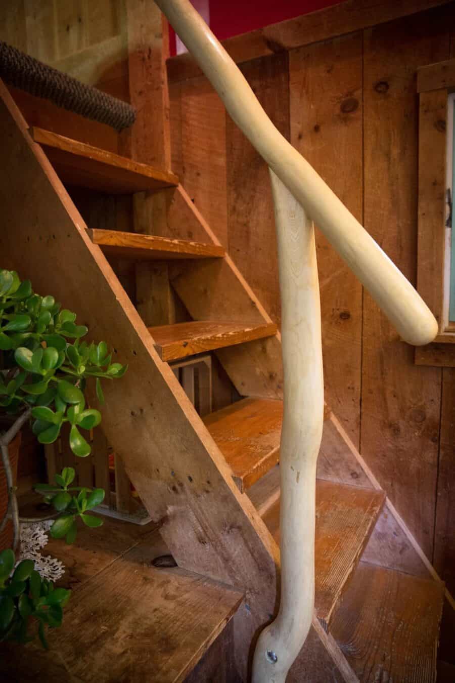 Wooden staircase inside a tiny cabin with natural wood walls and a unique curved handrail.