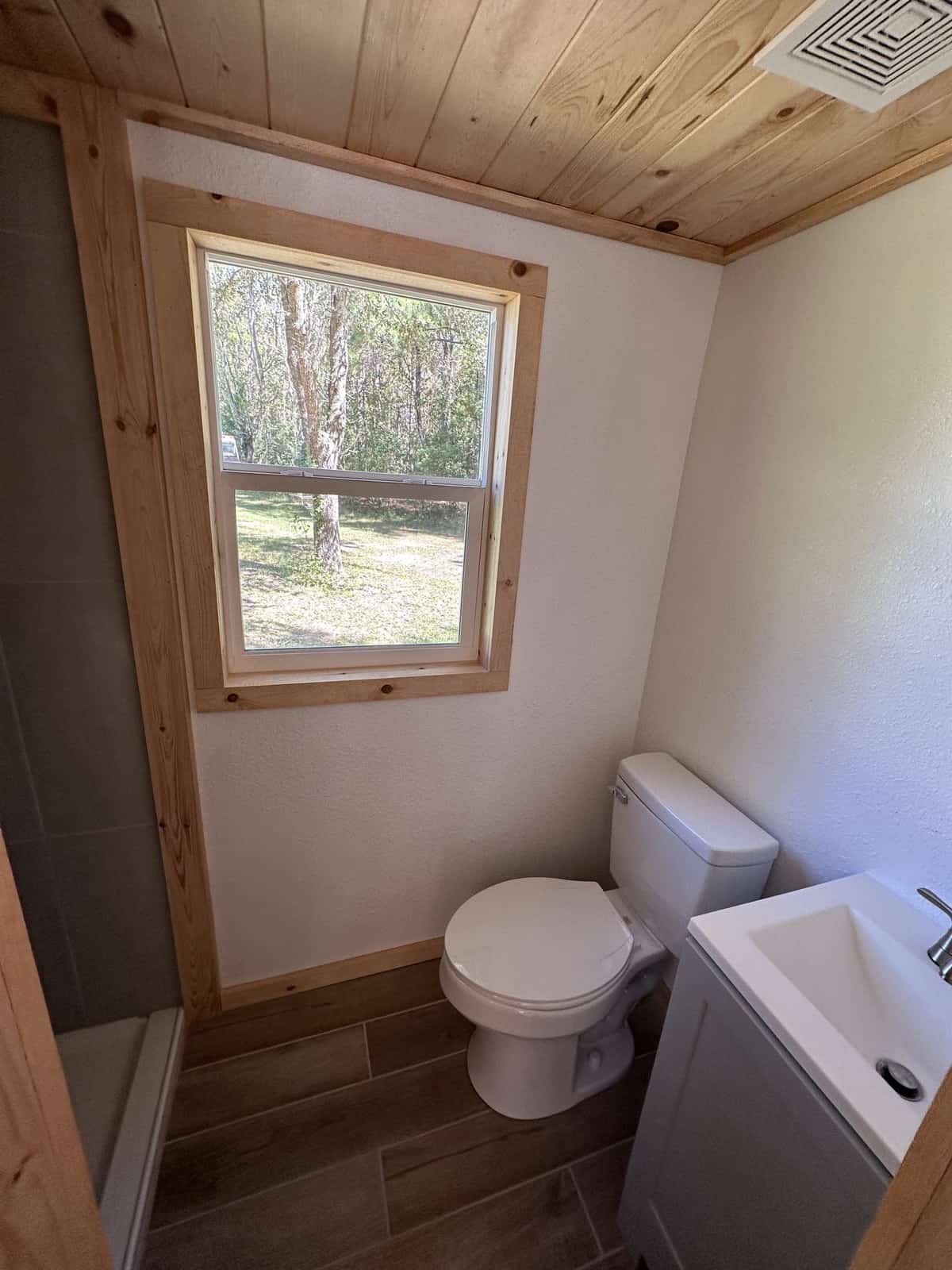 Full bathroom in the Shanti tiny house with a flush toilet, vanity, window, and a glimpse of the tiled shower
