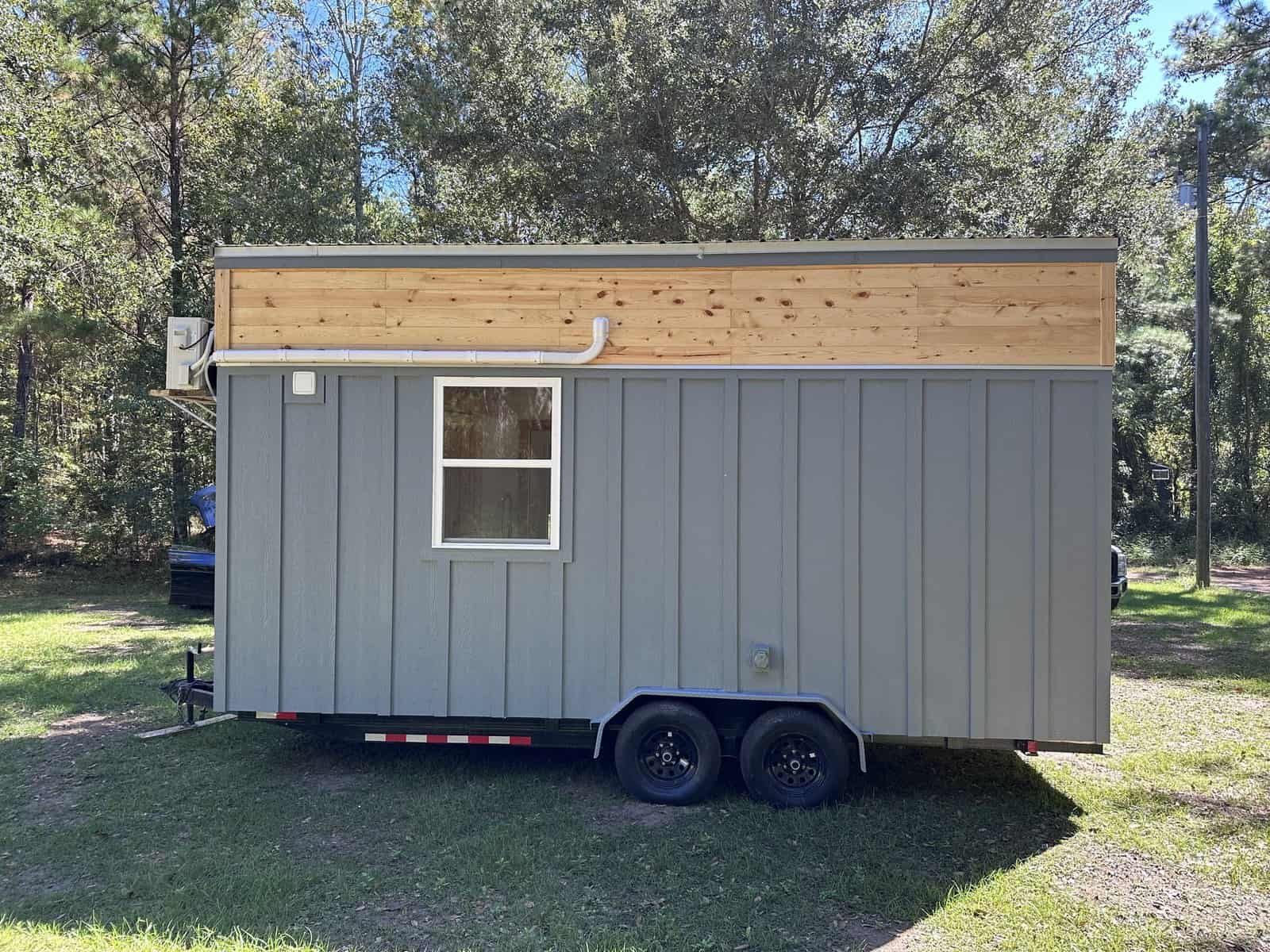 Side and rear view of the gray Shanti tiny house showing its long single-level body, cedar accent, and tandem-axle trailer