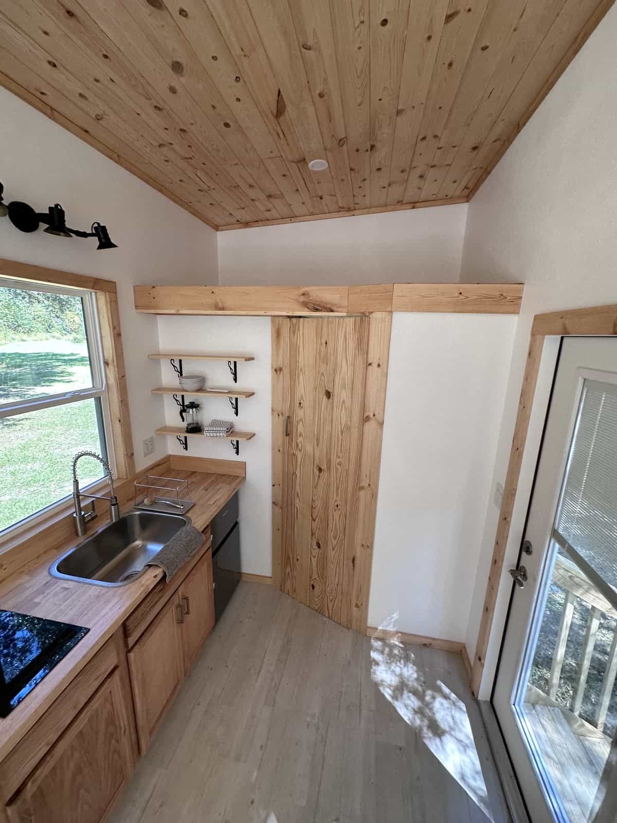 Shanti tiny house kitchen with oak cabinets, open shelving, and a pine tongue-and-groove storage closet beneath the loft