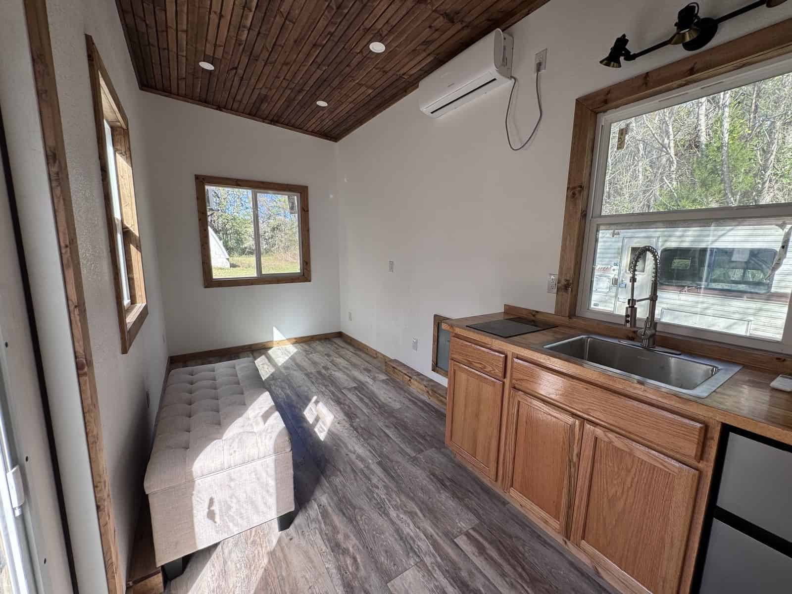 Shanti tiny house living area with a stained wood plank ceiling, a cushioned bench, the kitchen counter, and a mini-split heat pump