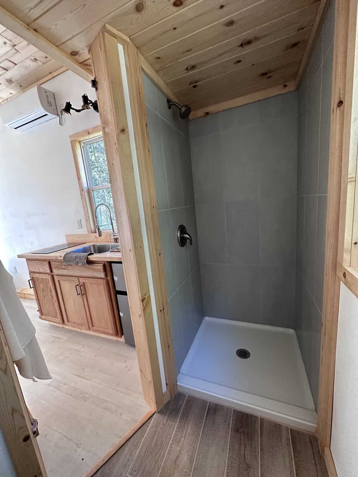 Tiled walk-in shower in the Shanti tiny house bathroom, with the kitchen visible through the open bathroom door