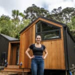 Modern tiny home with wooden exterior and connected porch in a lush forest setting.