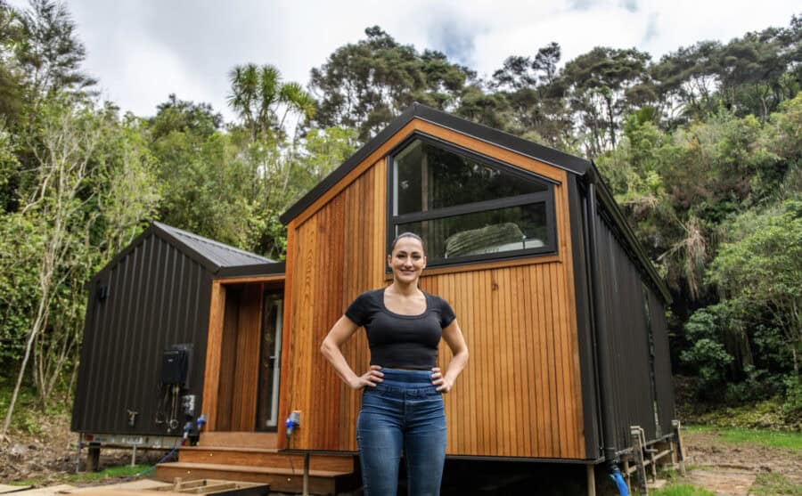 Modern tiny home with wooden exterior and connected porch in a lush forest setting.