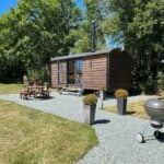 Shepherd's Hut tiny home with outdoor seating and grill on lush green land.