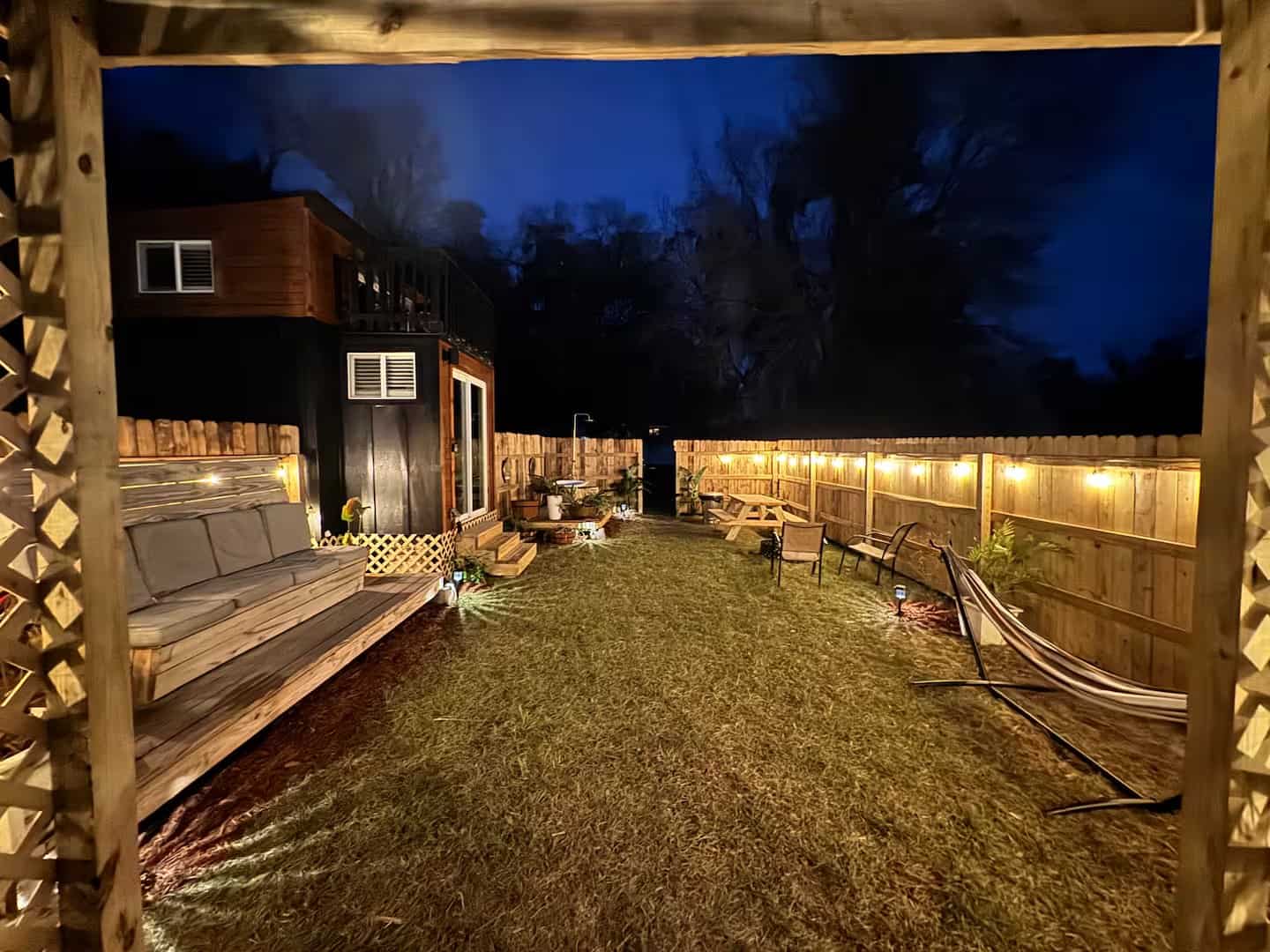 Shiva tiny home backyard at night with string lights, a hammock, and a daybed swing