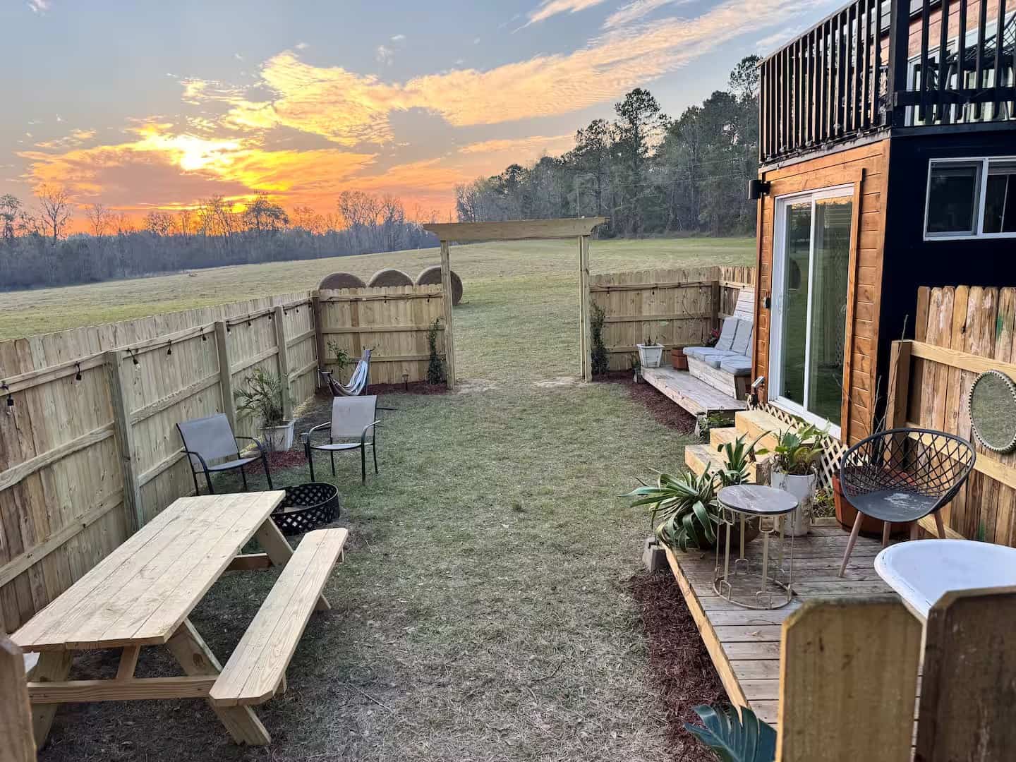 Private fenced backyard at sunset with a picnic table, fire pit, and open field views