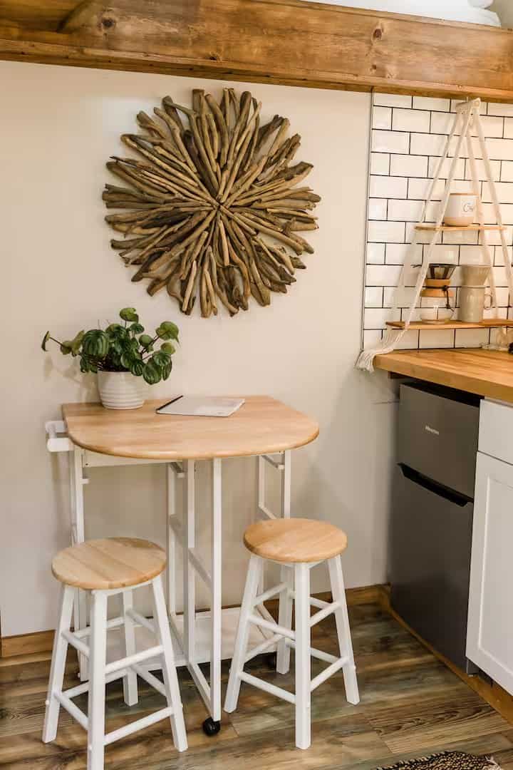 Fold-down dining table with two stools beneath a driftwood sunburst in the Shiva tiny home