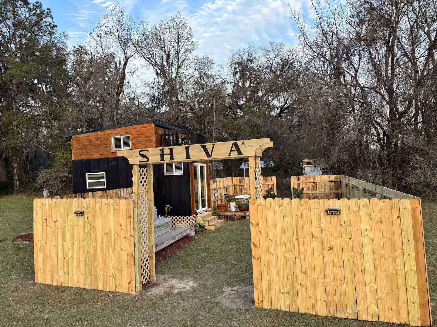 Shiva tiny home exterior with cedar and black board-and-batten siding and a SHIVA entrance arch over a private fenced yard