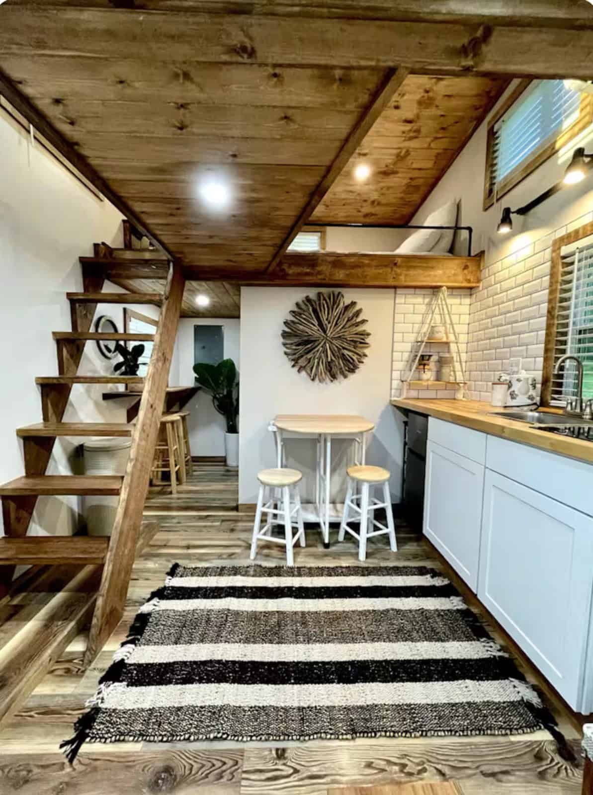 Open interior of the Shiva tiny home with loft stairs, dining nook, and kitchenette