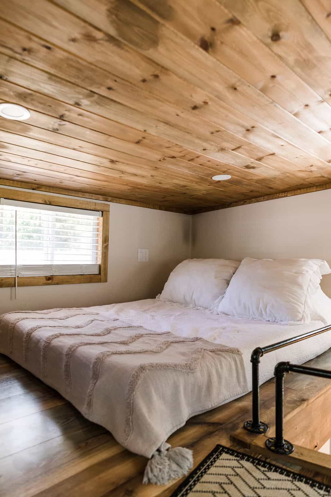 Queen bed in the knotty-pine sleeping loft of the Shiva tiny home
