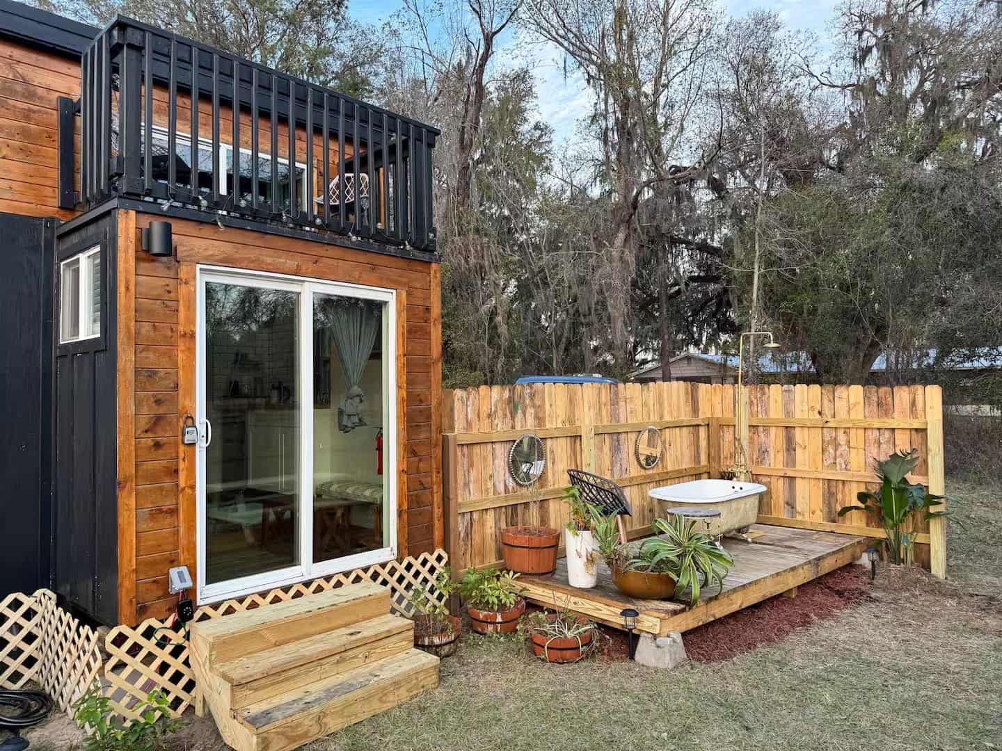 Side of the Shiva tiny home showing the sliding glass door, rooftop balcony, and a deck with an outdoor clawfoot tub