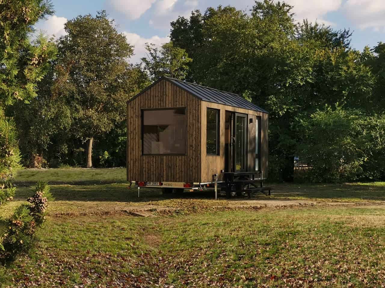Shoji tiny house parked in a grassy clearing surrounded by trees at golden hour, showing its compact 18-foot length on a double-axle trailer