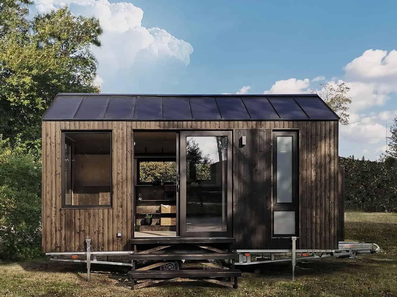 Front elevation of the Shoji tiny house showing sliding glass door open to reveal plywood shelving inside, plus a narrow frosted bathroom window
