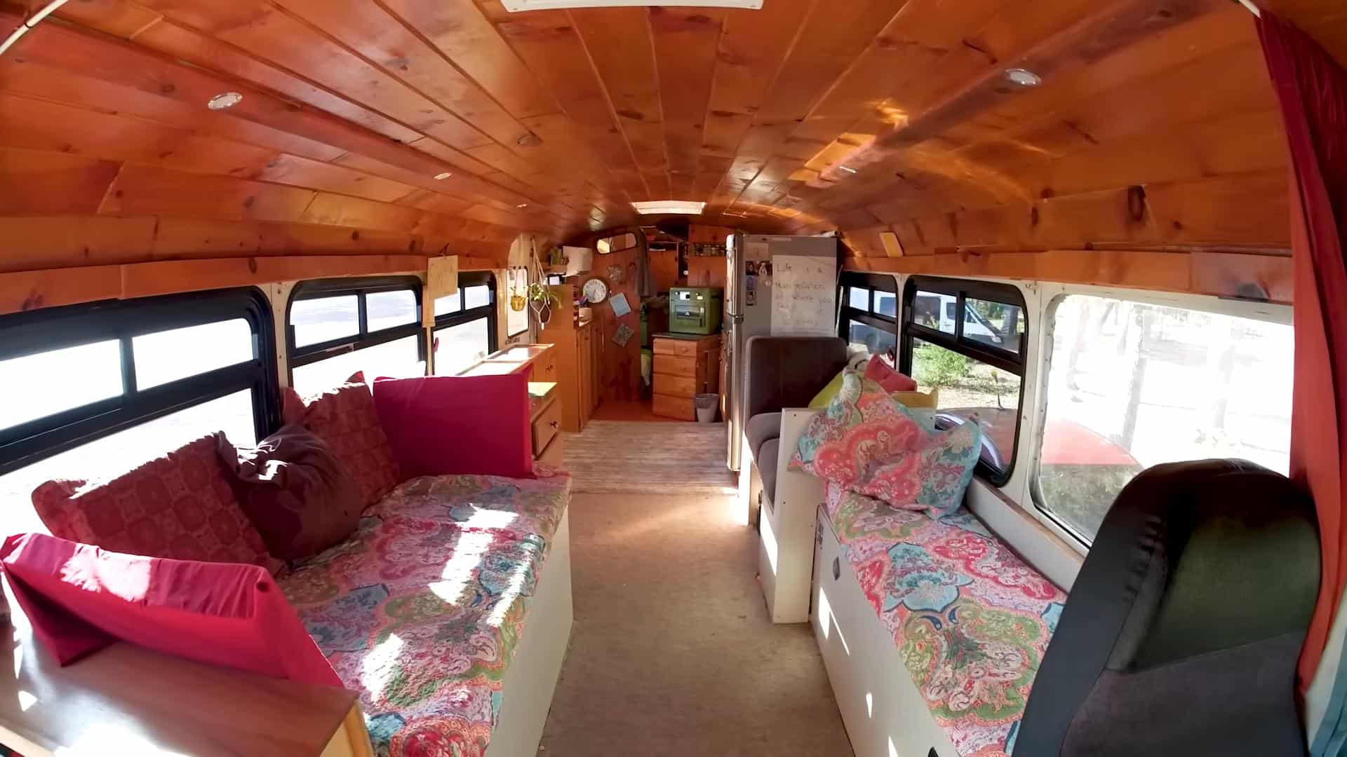 Interior of a tiny house bus with cozy seating, colorful cushions, and wooden ceiling.