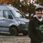 Skydiver standing next to a 4x4 Sprinter van in a scenic outdoor setting.