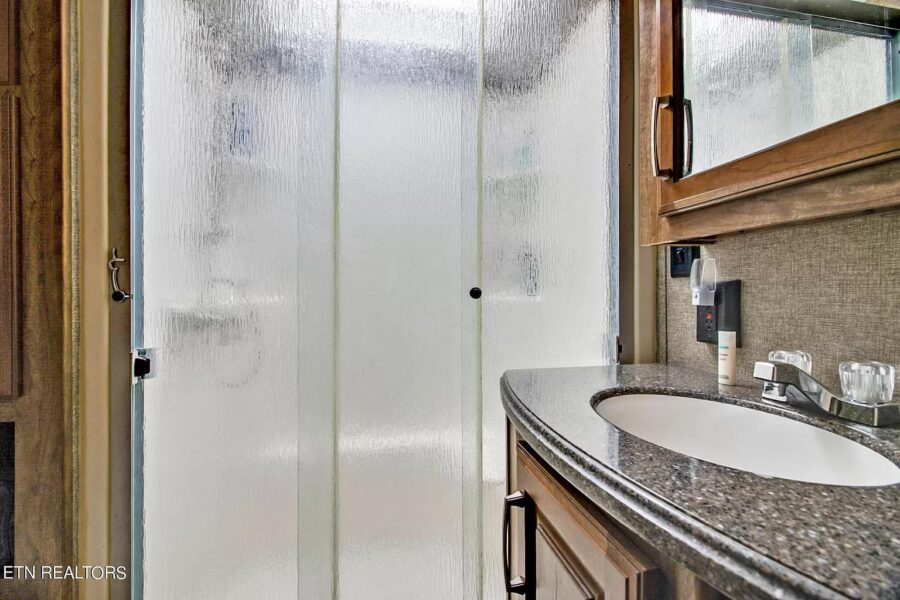 Compact bathroom with glass shower enclosure and wooden accents.