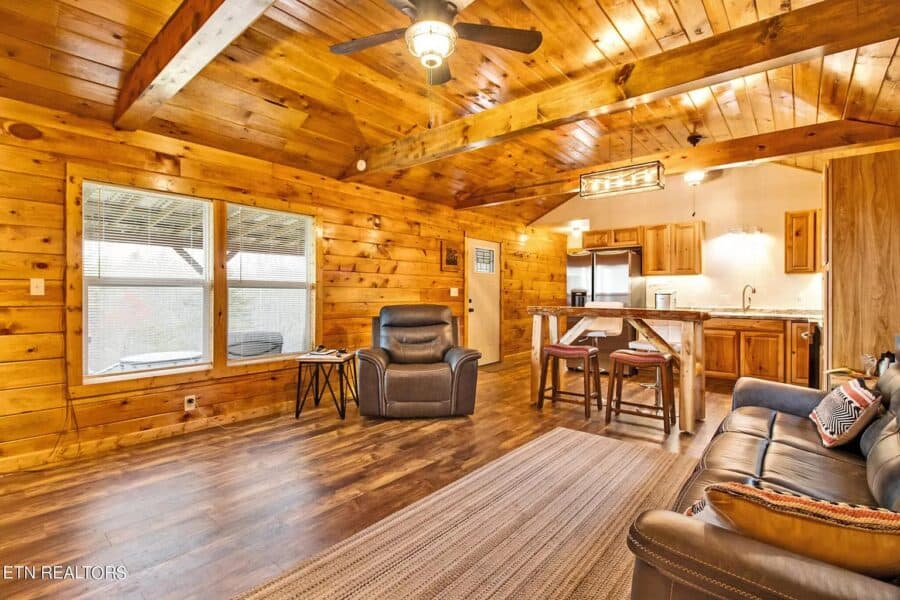 Charming tiny house living room featuring wood-paneled walls, large windows, and comfortable seating.