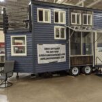 Modern tiny house on wheels with multiple windows and outdoor porch.