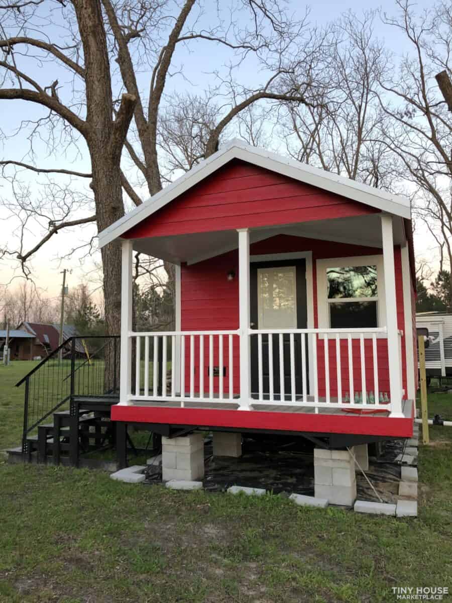 Small red cabin with porch on skids, ideal for tiny house living or getaway.