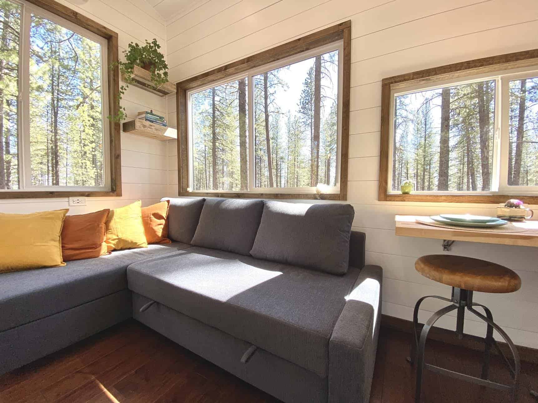 Spindrift Homes tiny house interior with an L-shaped couch and large windows overlooking pine trees