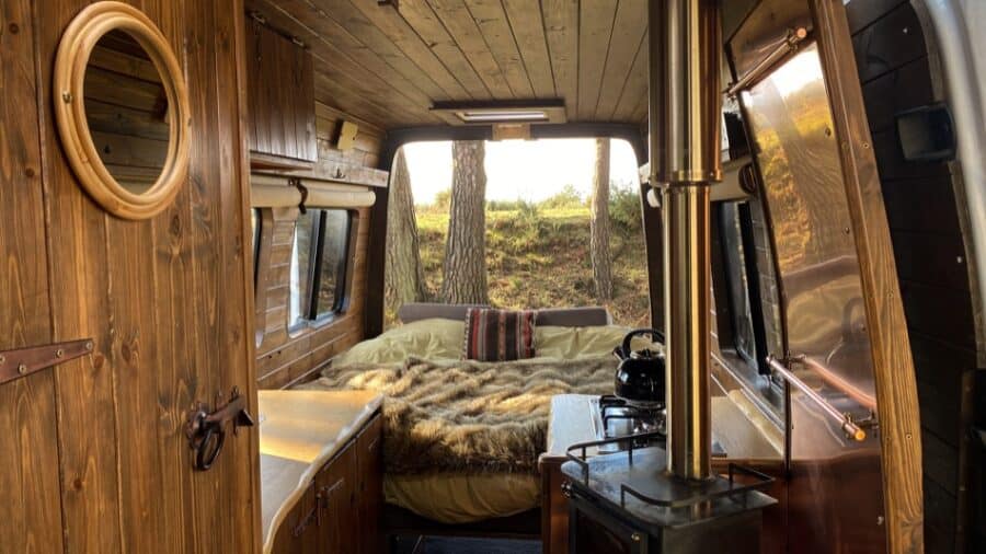Interior view of a cabin-inspired campervan with cozy bed and wooden decor.