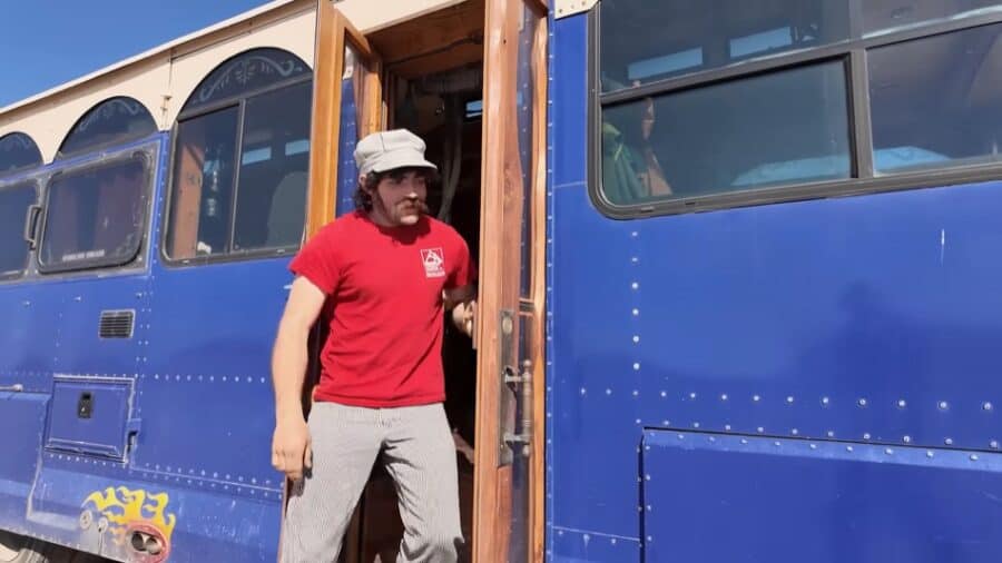 Man standing outside a converted blue trolley into a tiny home.