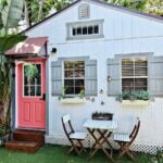 Small blue cottage with pink door and outdoor seating area.