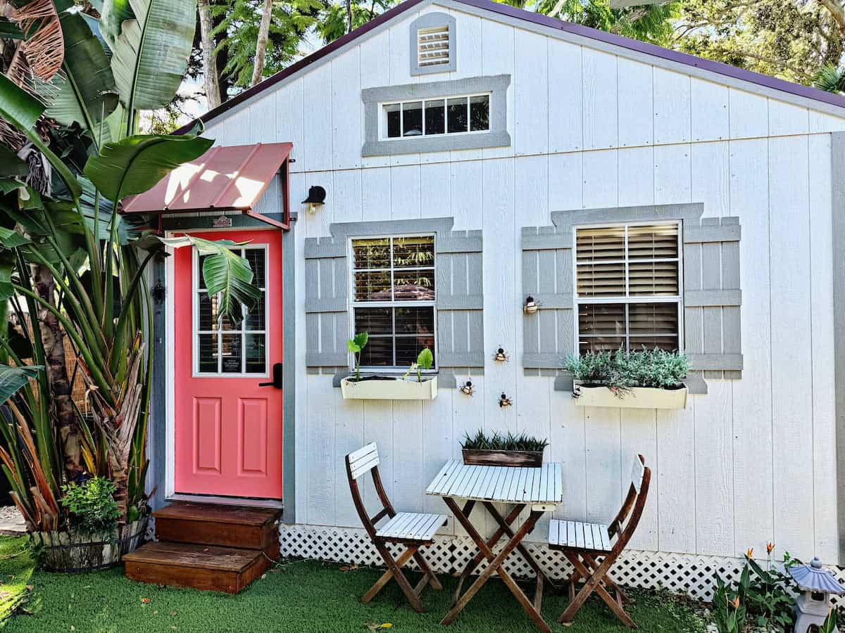 Small blue cottage with pink door and outdoor seating area.