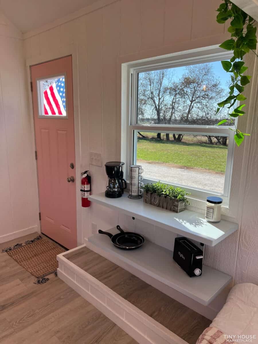 Bright tiny house interior featuring a compact kitchen with a window view of trees and outdoor scene.