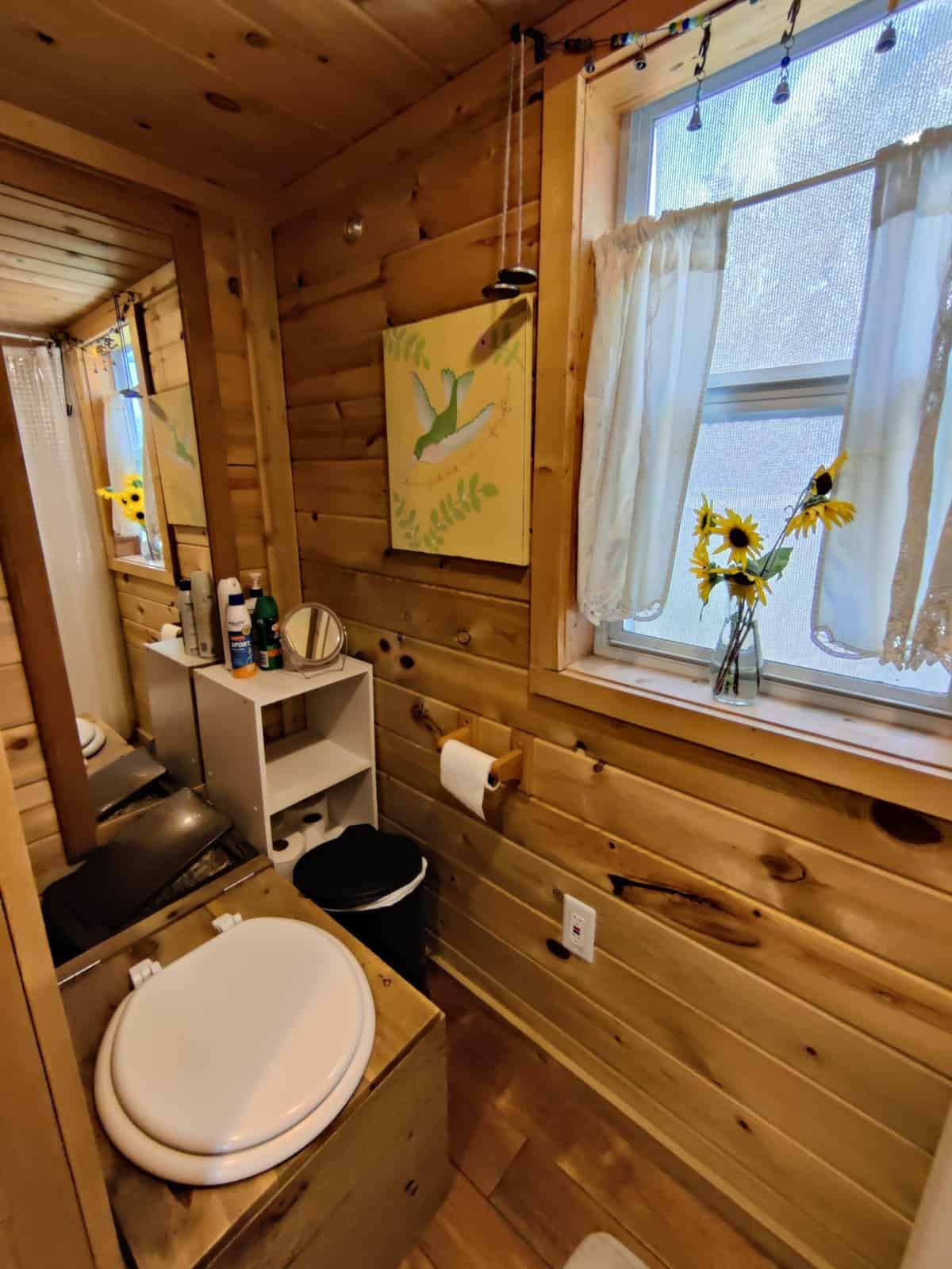 Bathroom with a composting toilet in a custom wooden enclosure and hummingbird artwork