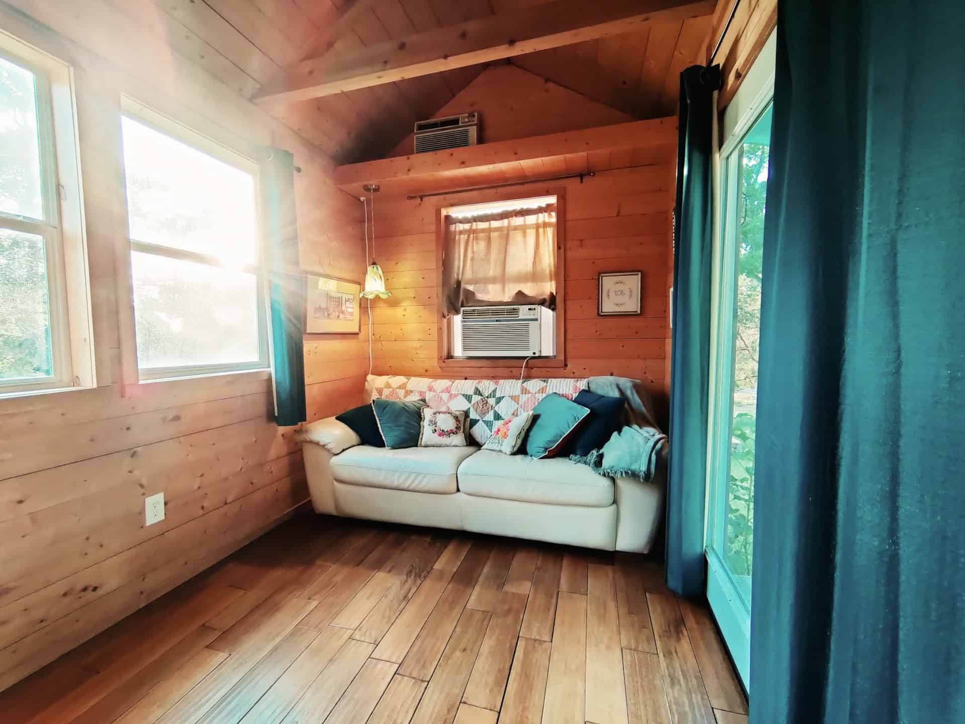 Cozy living room with a leather sofa, vaulted pine ceiling, and window air conditioner