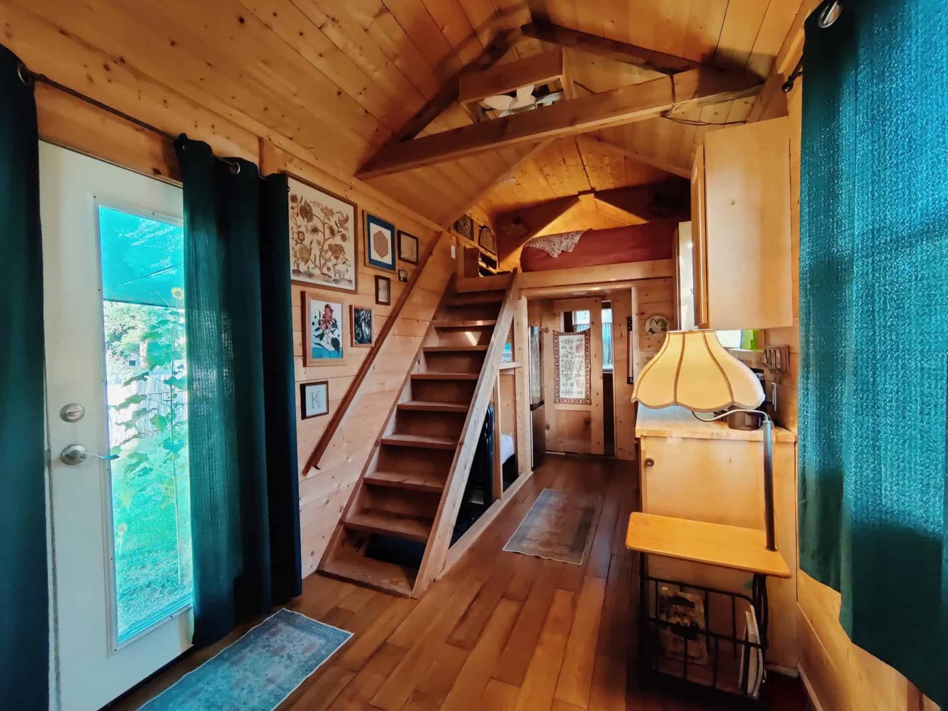 Interior of the Storybook Cedar tiny house showing the staircase to the loft, gallery wall, and glass door