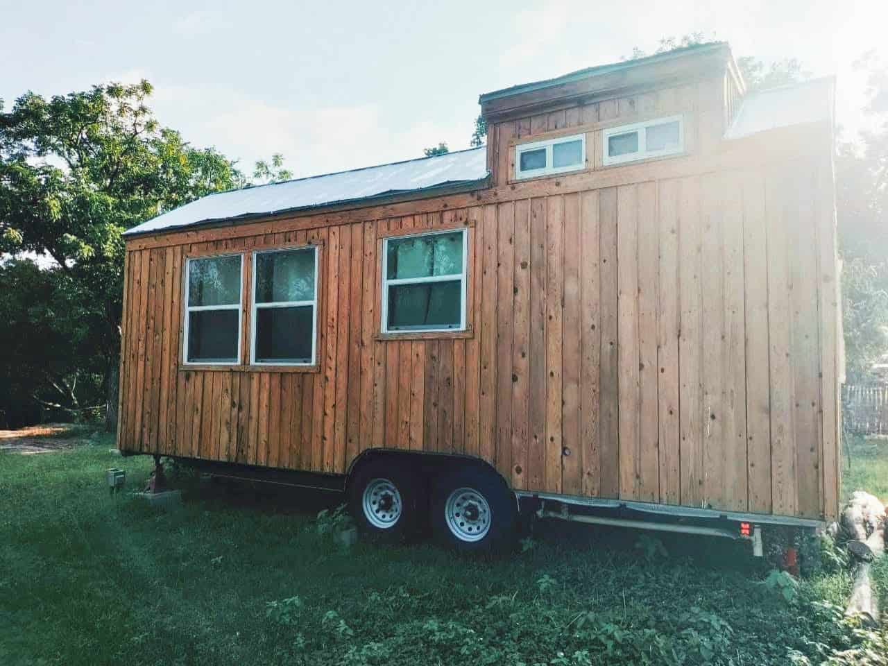 Side view of the Storybook Cedar tiny house showing its dual-axle trailer and dormer windows