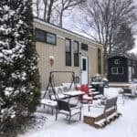 Tiny house with cozy outdoor seating in snowy landscape.