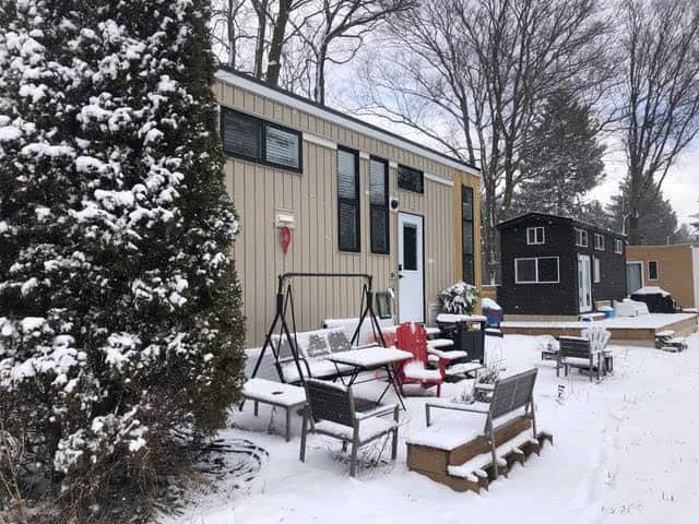 Tiny house with cozy outdoor seating in snowy landscape.